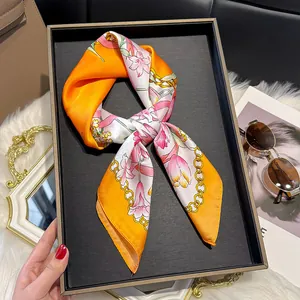 Detail of silk-like floral scarf with orange and pink lily patterns and golden chain accent