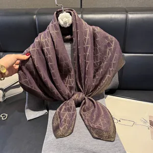 Close-up of deep purple silk scarf with metallic gold geometric patterns tied over grey knit