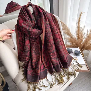 Detail of red paisley cashmere scarf with golden fringe drapes on a soft chair
