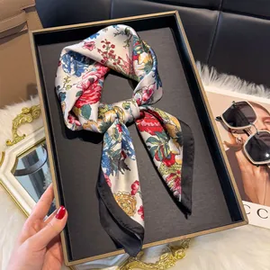 Dettaglio di sciarpa in seta a fiori, bordo nero e motivo vintage elegante su bianco