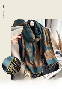 Detailed view of the dark green cashmere-like scarf showing paisley patterns and golden tassels