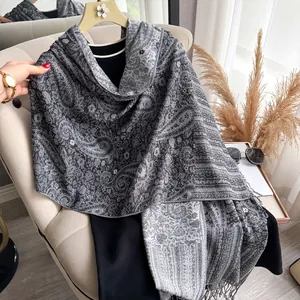 Detail van de grijze paisley-print en kwastjes aan de zijdeachtige sjaal voor dames