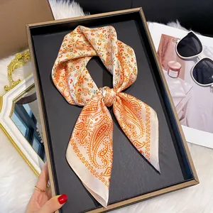 Gros plan d'un foulard en soie à motif paisley orange sur un plateau de luxe avec revues