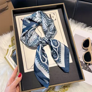 Detailopname van de marineblauw-witte zijden sjaal met paisleyprint op een zwart dienblad