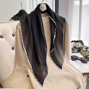Detail of black pleated silk scarf with white contrast edges on a beige knit sweater