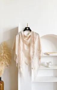 Detail showing elegant beige knit shawl with delicate lace flower patterns and long fringe