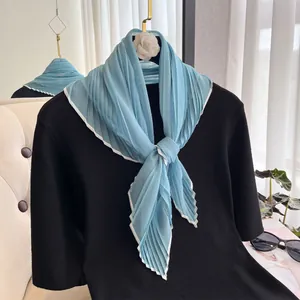 Close-up of pleated blue silk scarf with white borders on a chic black outfit