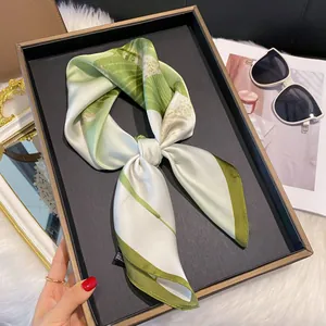 Détail d'un foulard en soie à imprimé botanique vert disposé sur un plateau noir