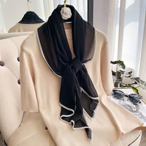 Close-up of pleated black neck scarf with white wavy trim on a beige knit top