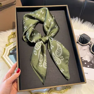 Dettaglio macro del foulard di seta verde scuro con motivo paisley su un vassoio nero