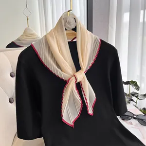 Close-up of pleated beige silk scarf with red edges paired with black knitwear top