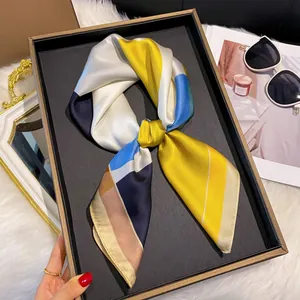 Détail d'un foulard en soie géométrique noué sur un plateau avec des accessoires