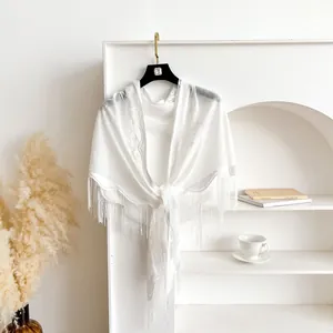 Detailed view of white lace triangle shawl featuring floral patterns and long tassels