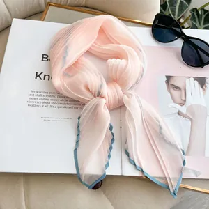 Pink pleated silk scarf with blue wavy edges on a fashion magazine with sunglasses