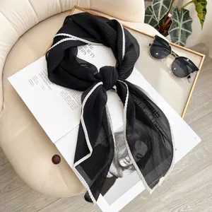 Elegant pleated black sheer scarf with white wavy edges on a stylish magazine