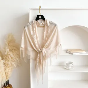 Detail of beige lace triangle shawl featuring hollow crochet patterns and fringe tassels