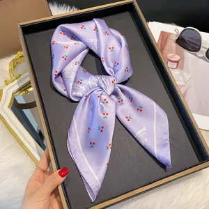 Gros plan d'un foulard en satin lilas avec motif cerise et paisley sur plateau
