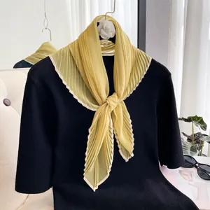 Detail of light yellow pleated silk scarf styled on a black knit top with stylish props