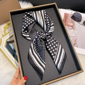 Gros plan d'un foulard en satin à pois noirs et blancs avec rayures en boîte cadeau