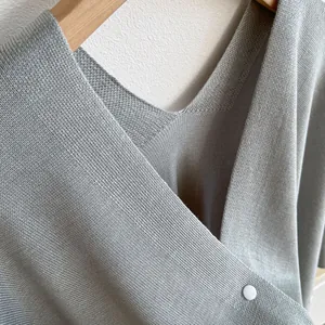 Détail d'un châle en maille gris clair avec col en V croisé et bouton blanc décoratif