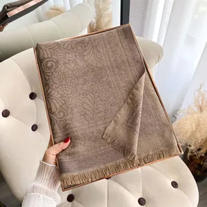 Dettaglio ravvicinato dello scialle marrone con jacquard dorato e bordo con nappe
