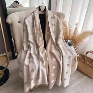 Macro detail of soft beige cashmere scarf featuring heart patterns and delicate tassel trim