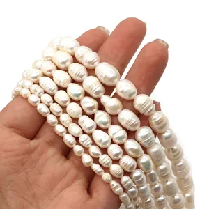 Brins de perles d'eau douce blanches de tailles variées tenus en main sur fond blanc épuré