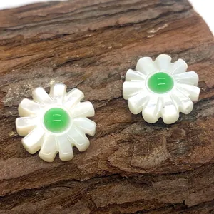 Close-up of daisy-shaped white shell beads with green gemstone centers on a wooden surface
