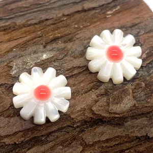 Macro shot of white daisy shell beads with red centers on a dark wood background