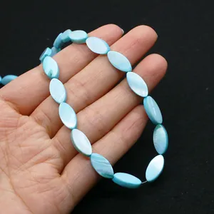 Détail de perles ovales en nacre bleu clair avec un éclat naturel tenues à la main