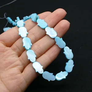 Détail macro de perles de nacre bleues en forme de Hamsa tenues dans la main