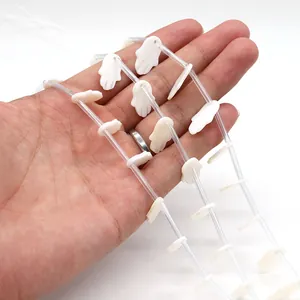 Detailed view of hand-shaped white shell beads held to show size and matte texture