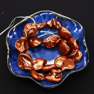 Macro shot of irregular bronze shell beads in a dark blue ceramic bowl for DIY jewelry
