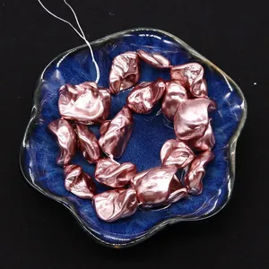 Detailed top view of rose gold irregular shell beads in a blue ceramic flower petal dish