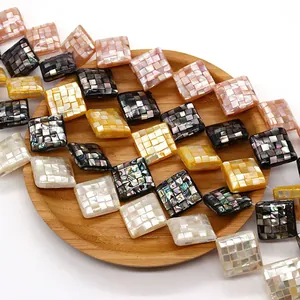 Mosaic shell beads in white black yellow and pink displayed on a round wooden tray