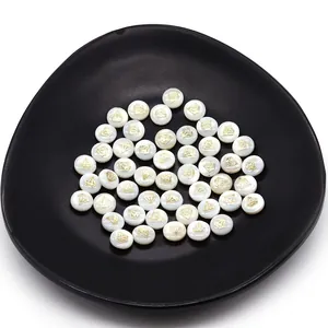 Detailed macro view of 6mm white shell beads with golden diamond pattern in a black tray