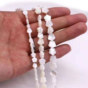 Natürliche weiße Muschelblumenperlen in drei Größen auf der Hand für DIY-Schmuckherstellung