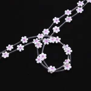 Detail view of 12mm white shell flower beads with purple oil drip on a clear string cord
