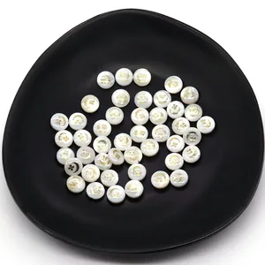 Macro shot of 6mm white shell beads with golden moon and floral patterns on black tray