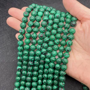 Dettaglio di perline tonde in malachite verde naturale con trame striate tenute in mano