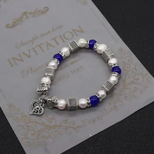 Dettaglio del bracciale di perle con perline blu e ciondolo a cuore su carta