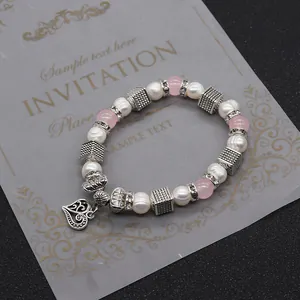 Dettaglio di un braccialetto di perle con ciondolo a cuore d'argento e perline rosa