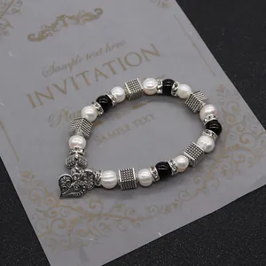 Dettaglio del bracciale di perle bianche e nere con un ciondolo a cuore argento