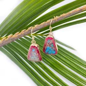 Detail of stone drop earrings with gold frame hanging on a green plant branch