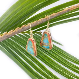 Detail of bohemian turquoise earrings with orange patterns hanging on a natural branch