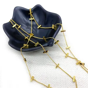 Goldene Kreuzkette mit rechteckigen Anhängern auf schwarzem Blumentablett für DIY Schmuck
