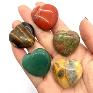 Five heart-shaped natural gemstones including tiger eye and jasper held in a hand