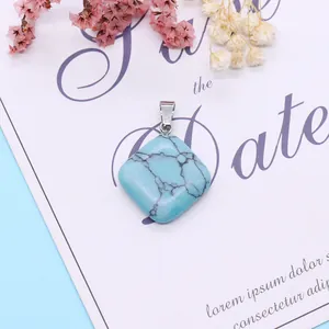 Rhombus turquoise stone pendant with silver clasp on white card with dried flowers