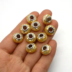Nahaufnahme von abakusförmigen Muschelperlen mit Mosaikmuster in der Hand für den Größenvergleich