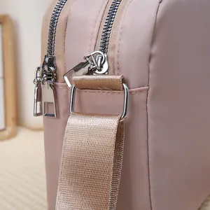 Detailed close-up of dual silver zippers and nylon fabric on pink crossbody bag